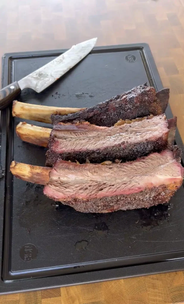 smoked beef ribs on a cutting board with a knife