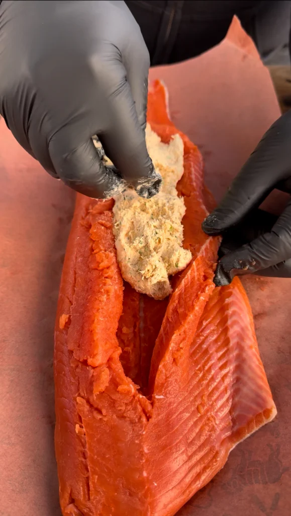 Crab stuffing being spooned into the pocket of a salmon fillet.