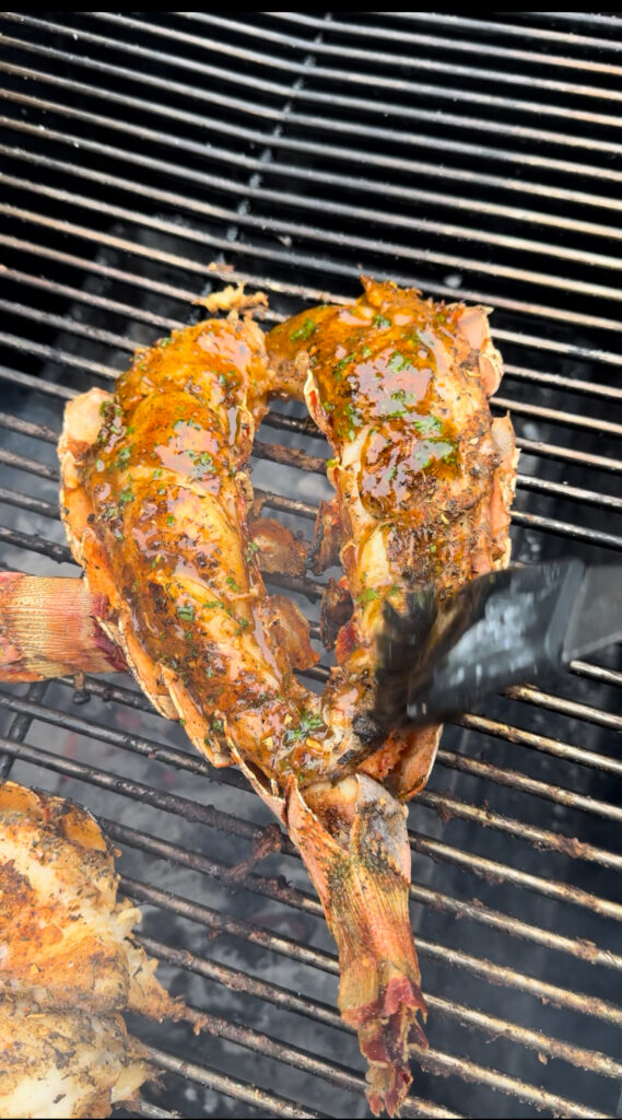 basting the cajun lobster tails on a grill with honey butter