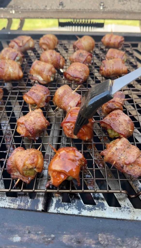 Brushing BBQ glaze over smoked chicken bacon pickle bites on the smoker