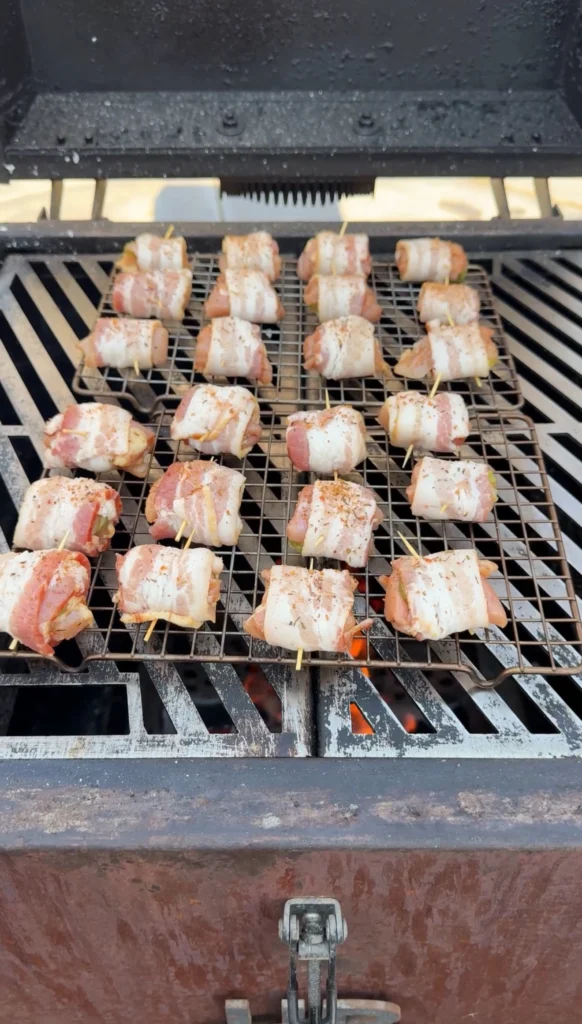 Chicken bacon pickle bites smoking on grill grates with rendered bacon