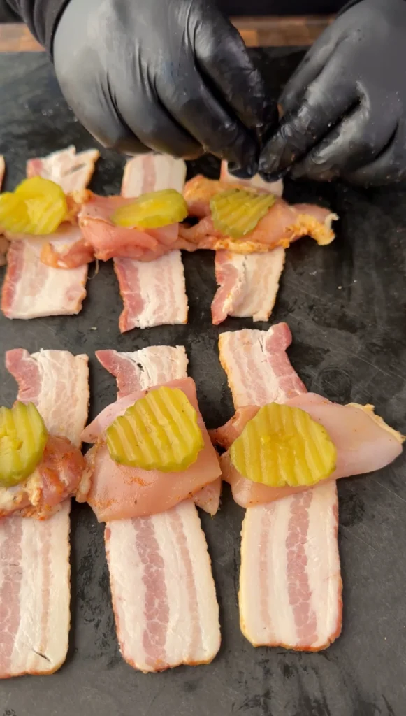 Halved thick-cut bacon slices laid out with dill pickle chips for assembly