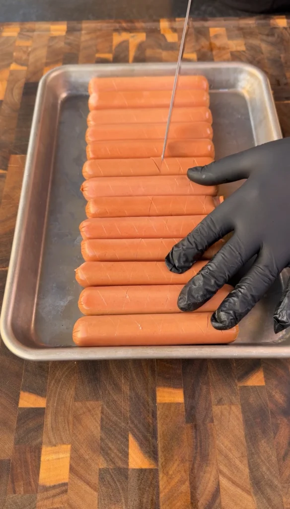Scored hotdogs with crosshatch cuts on a cutting board ready for seasoning