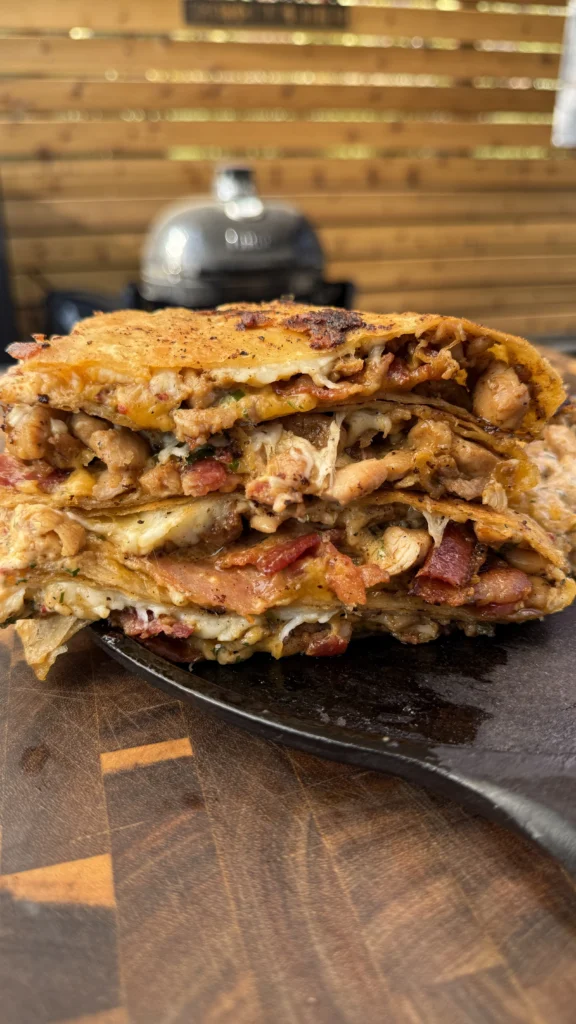 Close-up cross-section of loaded bacon chicken chipotle ranch quesadilla revealing melted cheese, seasoned chicken pieces, crispy bacon, and fresh herbs