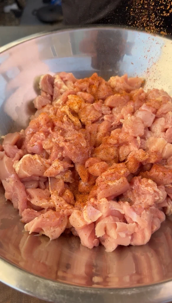Raw chicken thigh pieces in glass bowl generously coated with paprika and seasonings, prepared for cooking in bacon fat for quesadilla filling