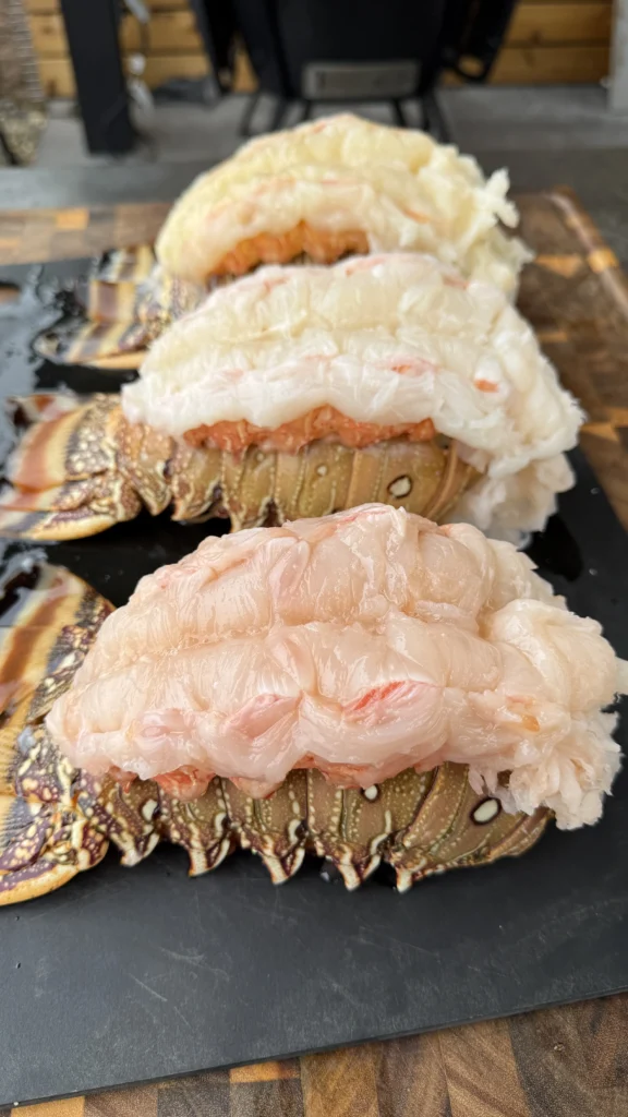 Raw lobster tails butterflied and prepared on slate board showing proper cutting technique with meat pulled through shell opening ready for smoking
