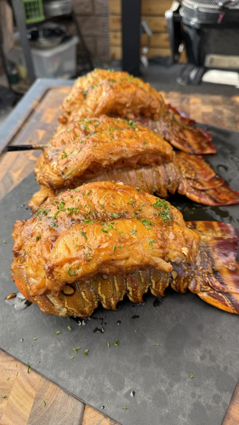 Smoked lobster tails with bourbon butter sauce on slate serving board, showing golden glazed meat, fresh parsley garnish, and caramelized shell presentation