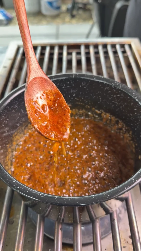 Smoky bourbon butter sauce simmering in black pan with wooden spoon, showing rich amber color and bubbling texture during cooking process