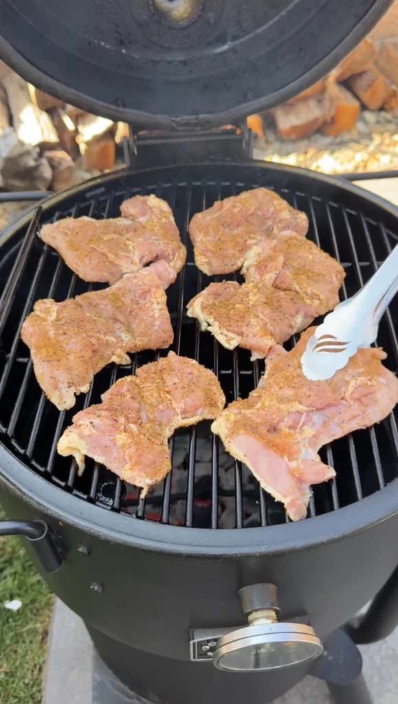 Raw chicken thighs seasoned with Danos Cheesoning placed on round grill grates, showing proper preparation before cooking begins