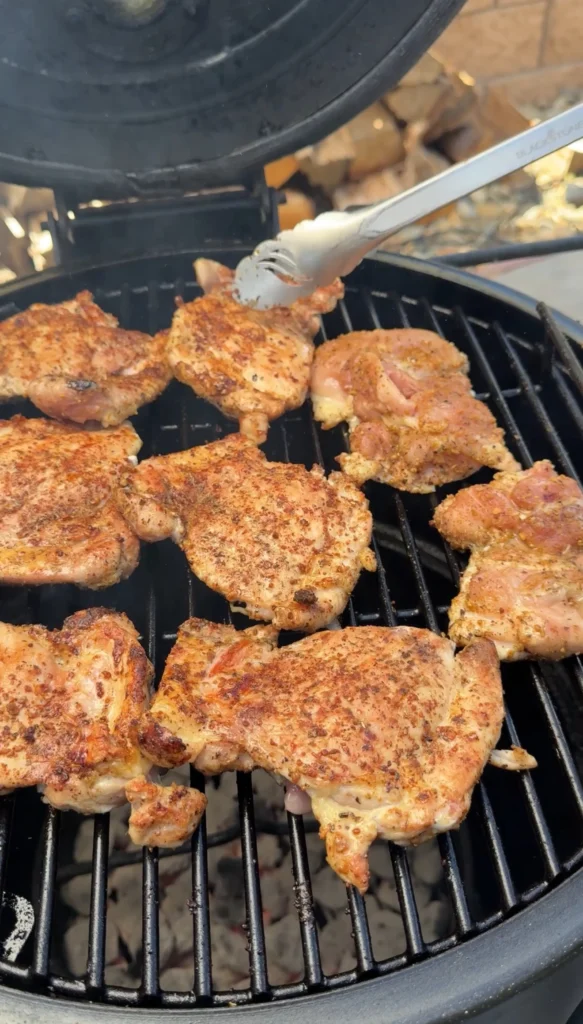 Grilled chicken thighs being checked for doneness with tongs on grill grates, showing proper golden-brown color and grill marks