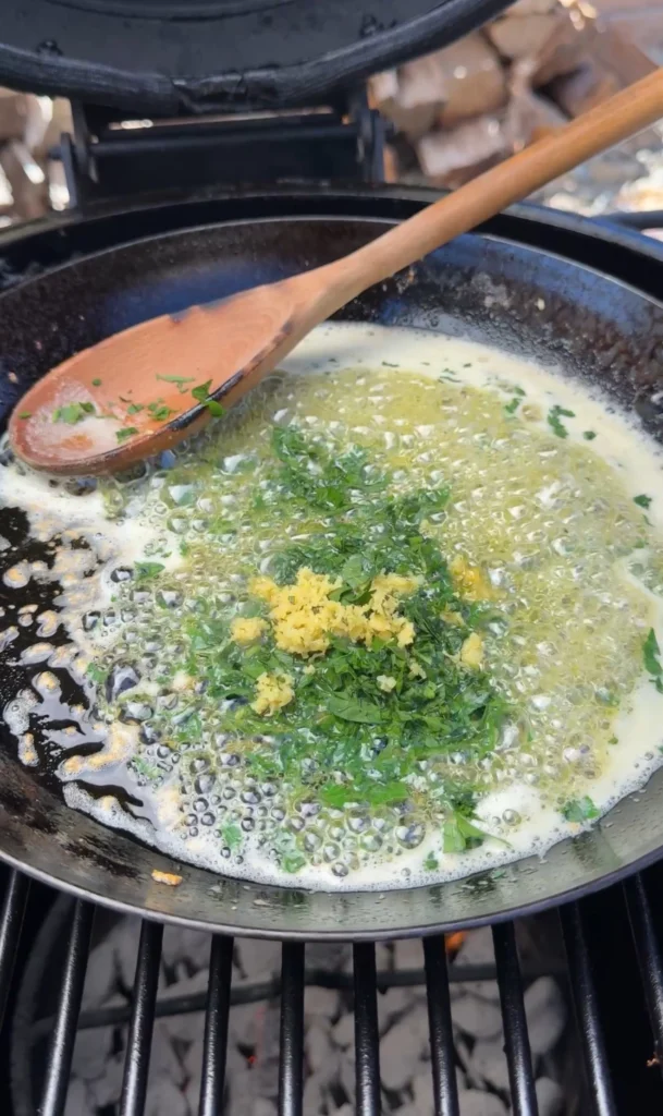 Garlic herb butter sauce being prepared in cast iron skillet with melted butter, fresh herbs, lemon zest, and minced garlic visible