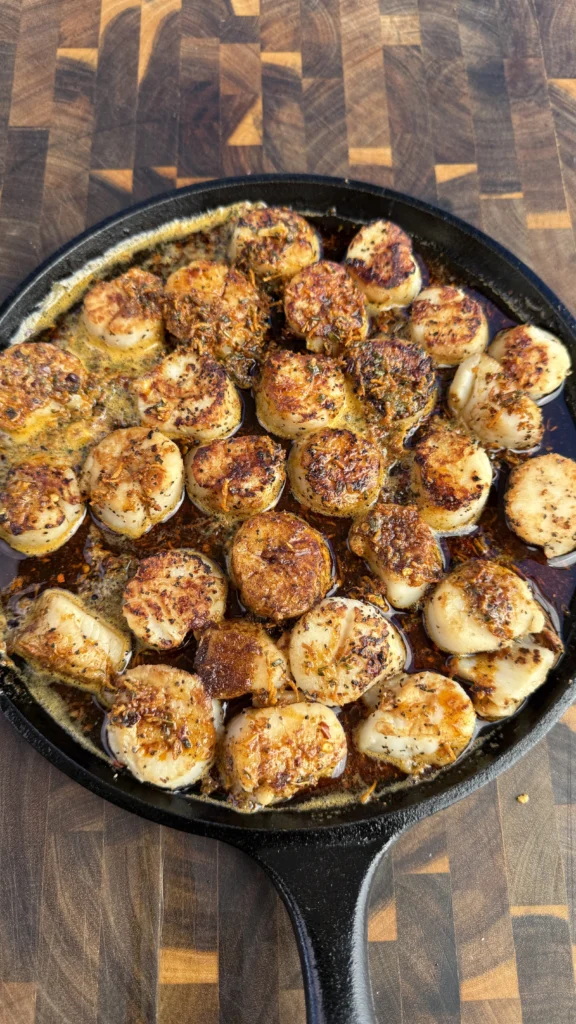Golden-brown seared scallops in cast iron skillet with cowboy butter sauce, showing perfect caramelization and herb-flecked butter coating