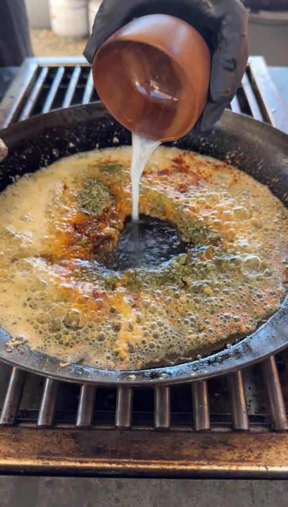 Melted cowboy butter being poured into cast iron skillet with herbs and spices visible, creating aromatic pan sauce for scallops