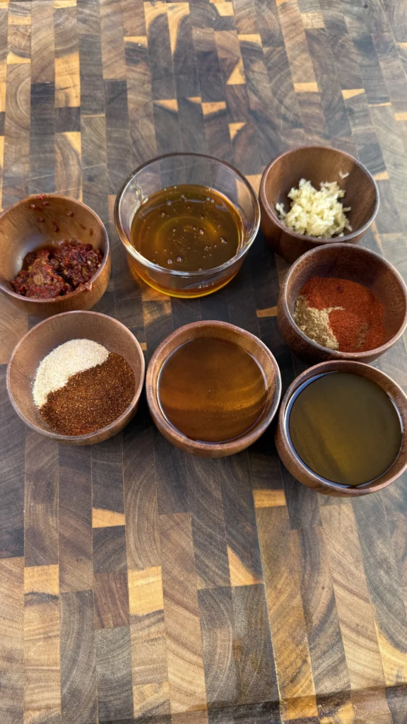 Individual honey chipotle sauce ingredients in wooden bowls showing chipotle peppers, honey, spices, garlic, and olive oil for chicken marinade