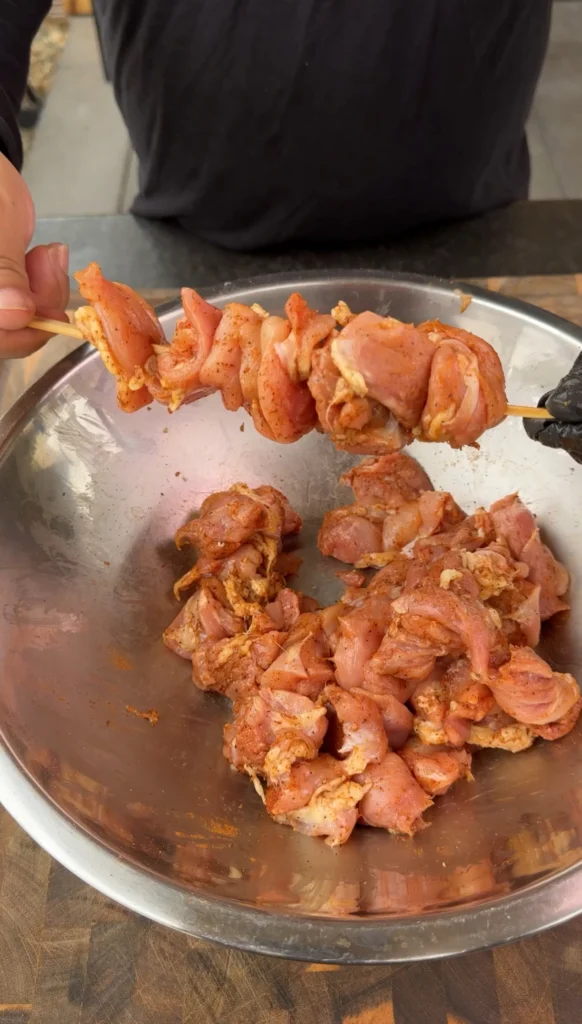 chicken being placed on a wooden skewer