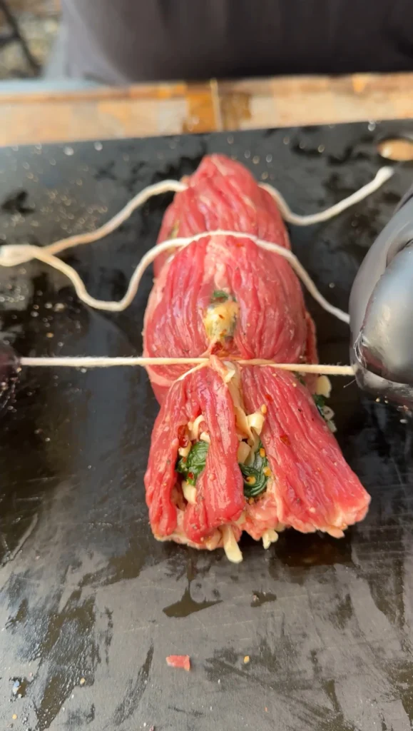 wo tied skirt steak rolls secured with kitchen twine on grill grates, showing proper preparation before slicing into pinwheels