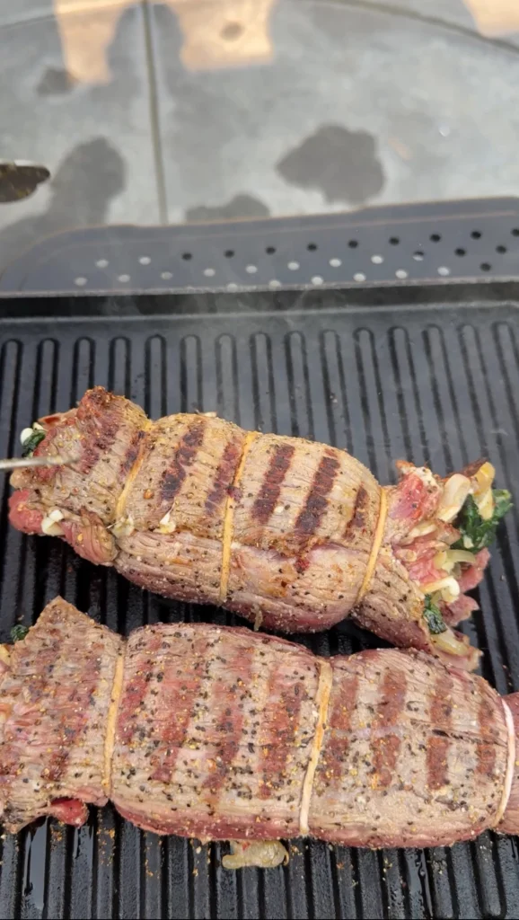 Two tied skirt steak rolls secured with kitchen twine on grill grates, showing proper preparation before slicing into pinwheels