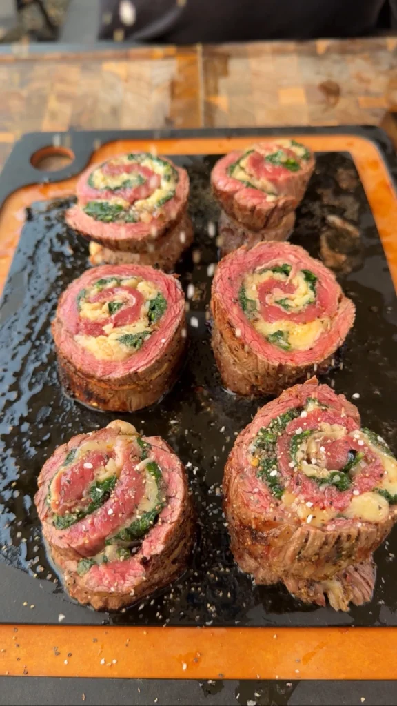 Sliced chili oil steak pinwheels on grill grates showing perfect spiral pattern with spinach and melted cheese filling
