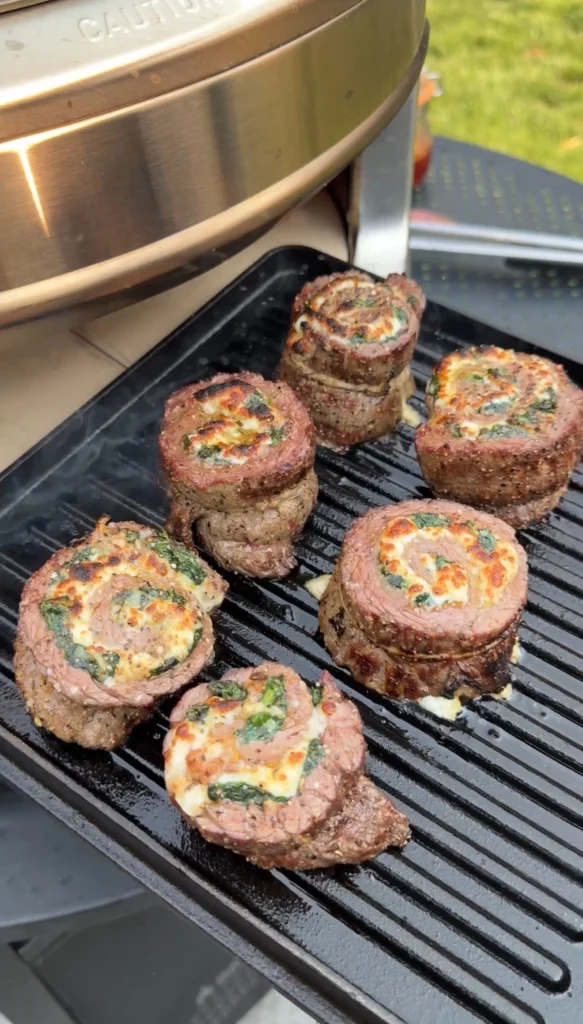Sliced chili oil steak pinwheels on grill grates showing perfect spiral pattern with spinach and melted cheese filling