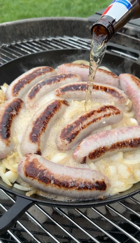 beer being poured into a cast iron with brats