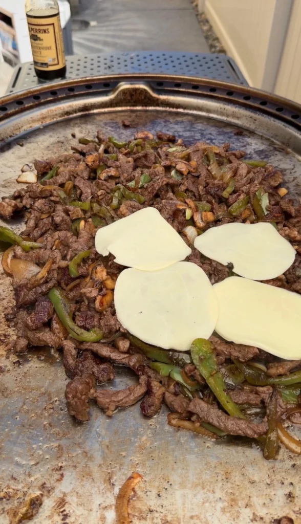cheesesteak ingredients being cooked on the griddle