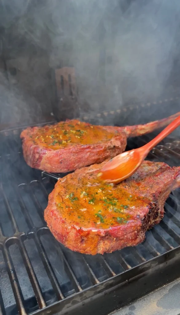 adding garlic butter to the steaks on the grill