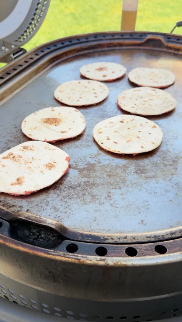 Hand pressing beef flat across a flour tortilla on a hot flat top griddle at 400°F