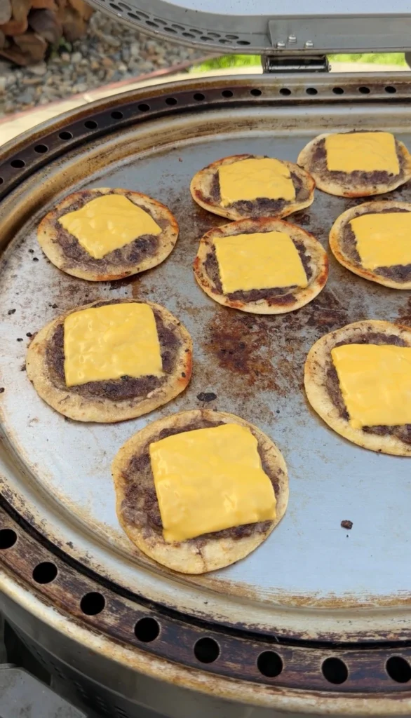 Hand pressing beef flat across a flour tortilla on a hot flat top griddle at 400°F