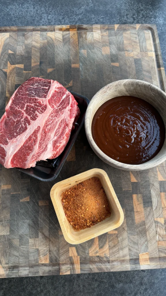 Raw chuck roast with BBQ sauce and seasoning rub on a cutting board
