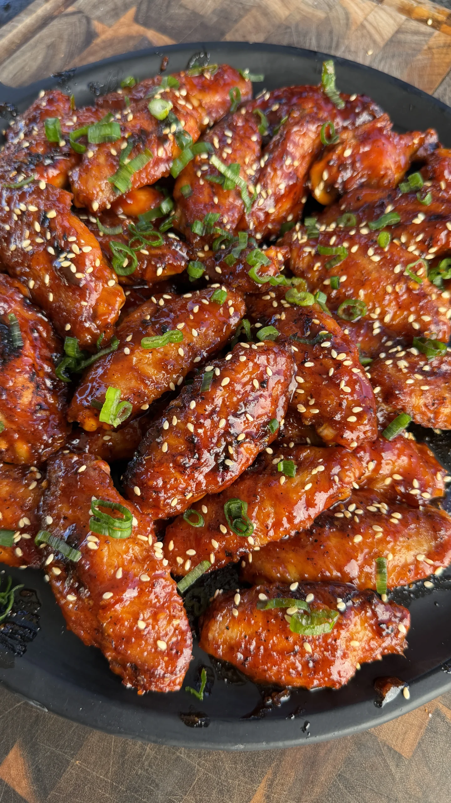 Finished grilled gochujang chicken wings with glossy red sauce, sesame seeds, and sliced scallions on a dark plate