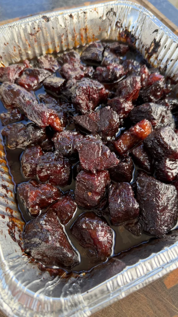 Finished chuck roast burnt ends with sticky caramelized glaze in a foil pan