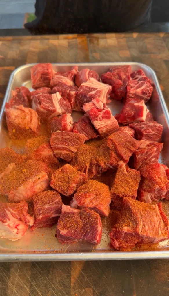 Cubed chuck roast with BBQ rub on a sheet pan ready for the smoker