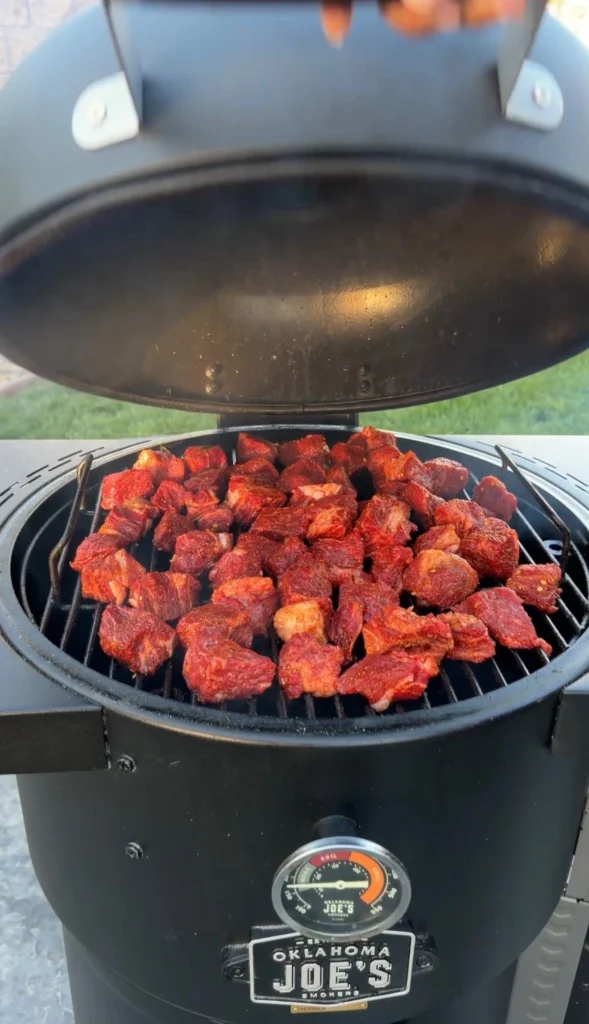 Seasoned chuck roast cubes smoking on an Oklahoma Joe's smoker