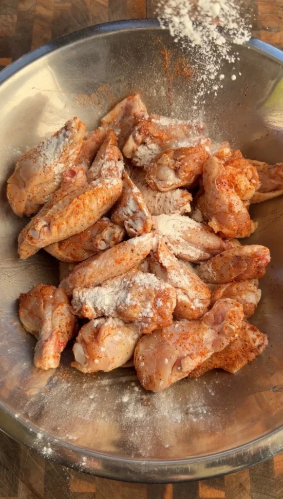 Split chicken wings tossed with paprika seasoning and flour in a stainless steel mixing bowl
