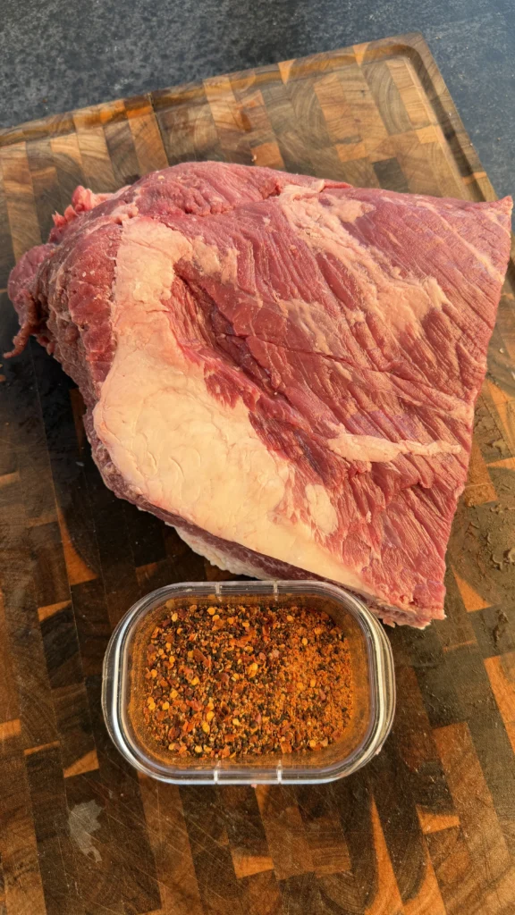 Raw brisket point with BBQ seasoning rub in a container on a cutting board