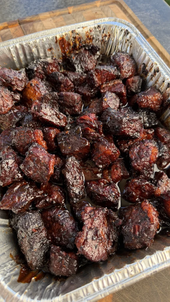 Close-up of finished smoked brisket burnt ends with deep dark sticky glaze in a foil pan