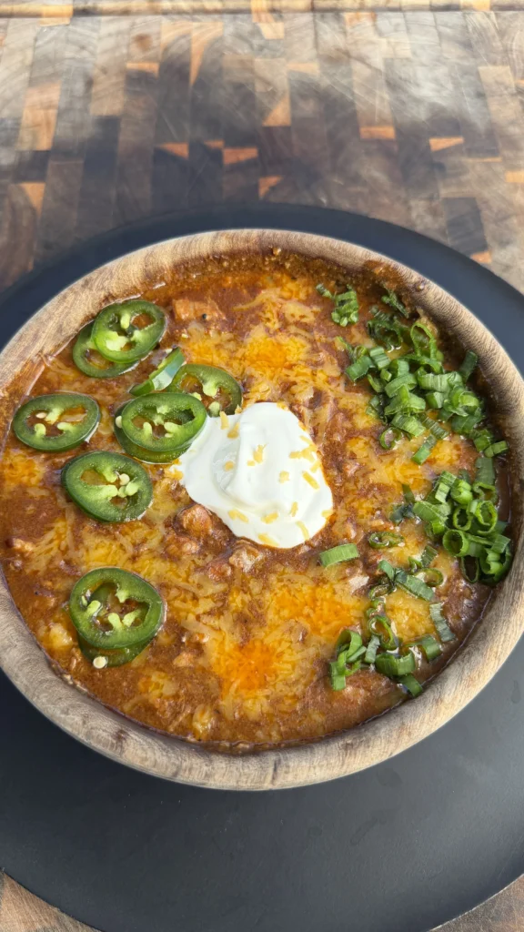Bowl of smoked brisket chili topped with sour cream, melted cheddar, sliced jalapeños, and green onions