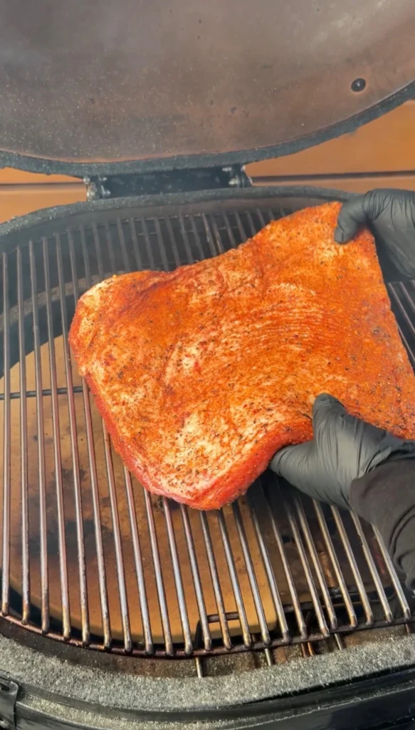 Seasoned brisket flat being placed on a kamado grill for smoking