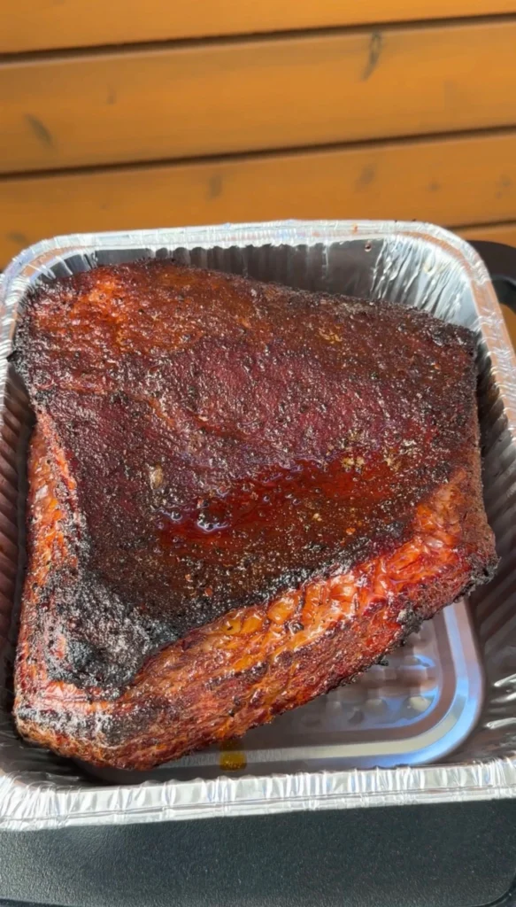 Smoked brisket flat with deep dark bark resting in a foil pan