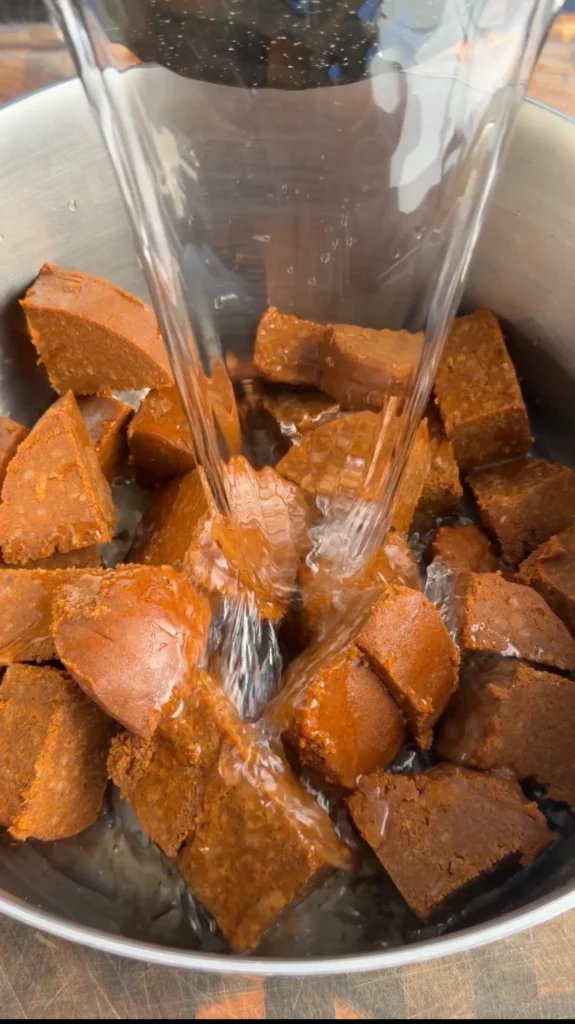 Water being poured over cubed chili con carne base in a steel bowl