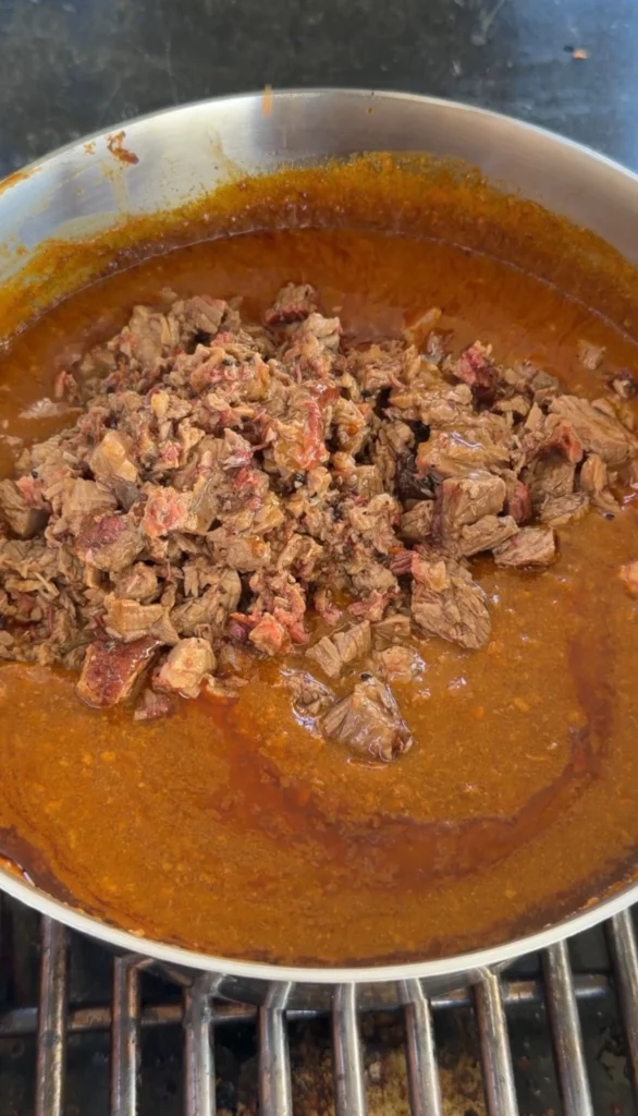 Chopped smoked brisket simmering in chili sauce in a pan on the stovetop