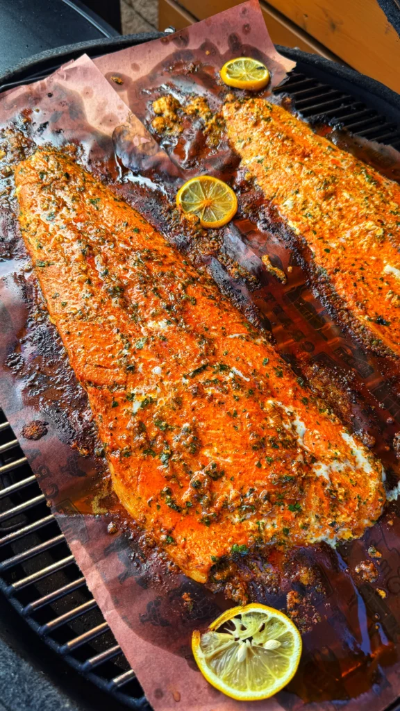 Two finished smoked salmon fillets on butcher paper with caramelized garlic herb butter and lemon slices on a grill