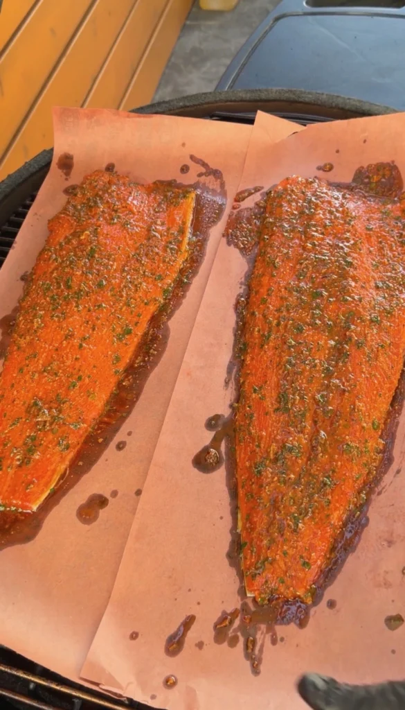 Wooden spoon spreading lemon pepper garlic herb butter mixture over a scored raw salmon fillet on butcher paper