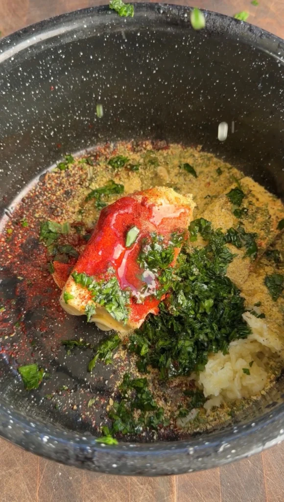 Close-up of garlic herb butter mixture with melted butter, parsley, paprika, garlic, and lemon pepper seasoning in a dark bowl