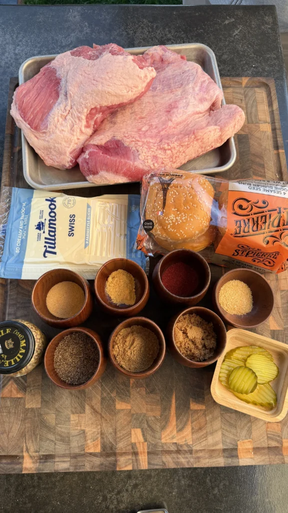 Raw corned beef on a tray with Tillamook Swiss cheese, brioche buns, spice rub bowls, mustard, and pickles on a cutting board