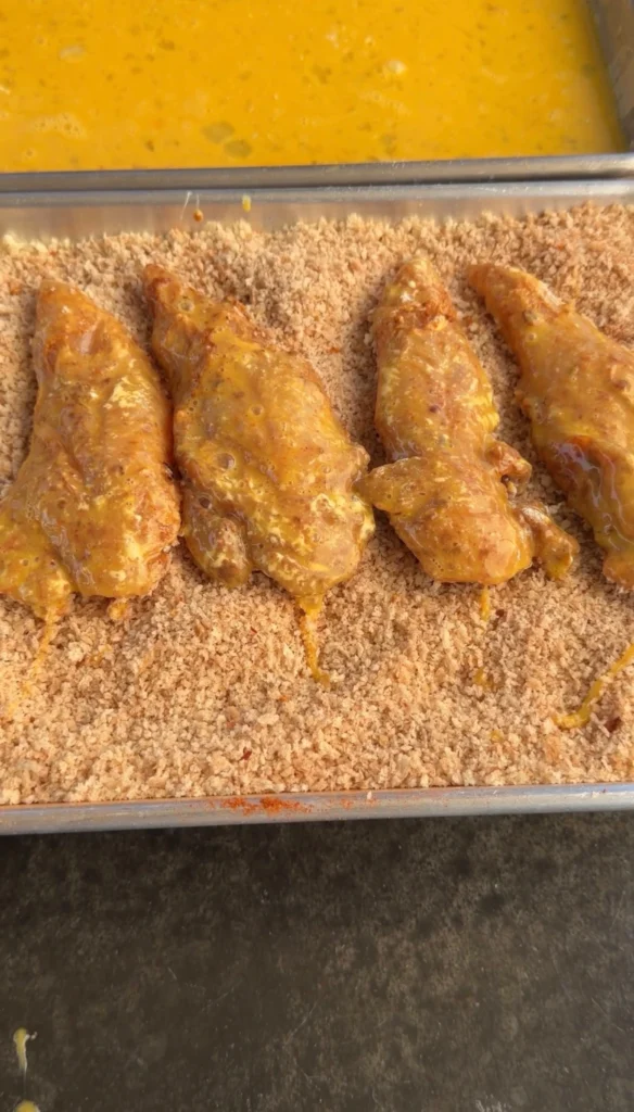 Egg-washed chicken tenders sitting in a tray of panko breadcrumbs ready for coating