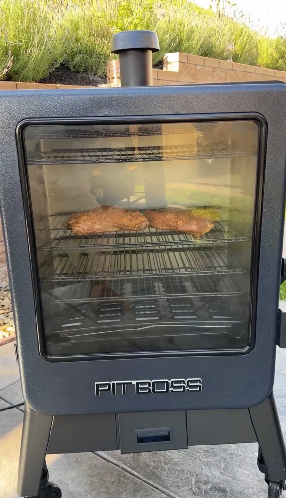 Seasoned corned beef smoking inside a Pit Boss vertical smoker through the glass window