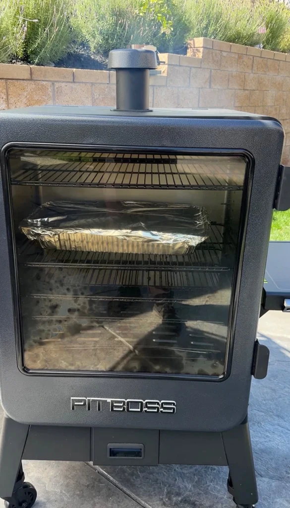 Foil-covered pan of pastrami braising inside a Pit Boss vertical smoker