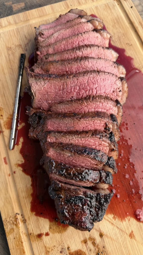 Sliced picanha steak showing perfect medium-rare pink interior with juices on a cutting board