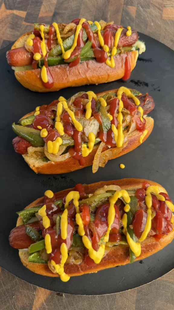 Three bacon-wrapped chile relleno hot dogs on slate plate drizzled with yellow mustard and red sauce